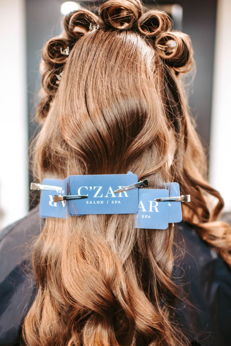 Formal special occasion hairstyle prep. Long brunette hair with a soft wave and C'zar Salon business cards used as setting props.