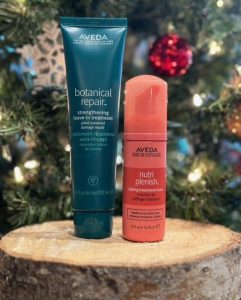 aveda gifts with purchase: two aveda beauty products on a wooden log in front of a lit evergreen tree